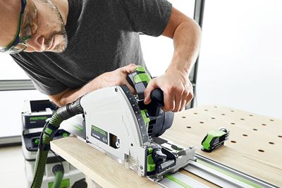 Vīrietis ar Festool ripzāģi zāģē dēli uz daudzfunkcionālā galda