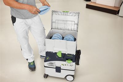 Amatnieks stāv blakus Systainer kastei, kas piepildīta ar slīpēšanas materiāliem
