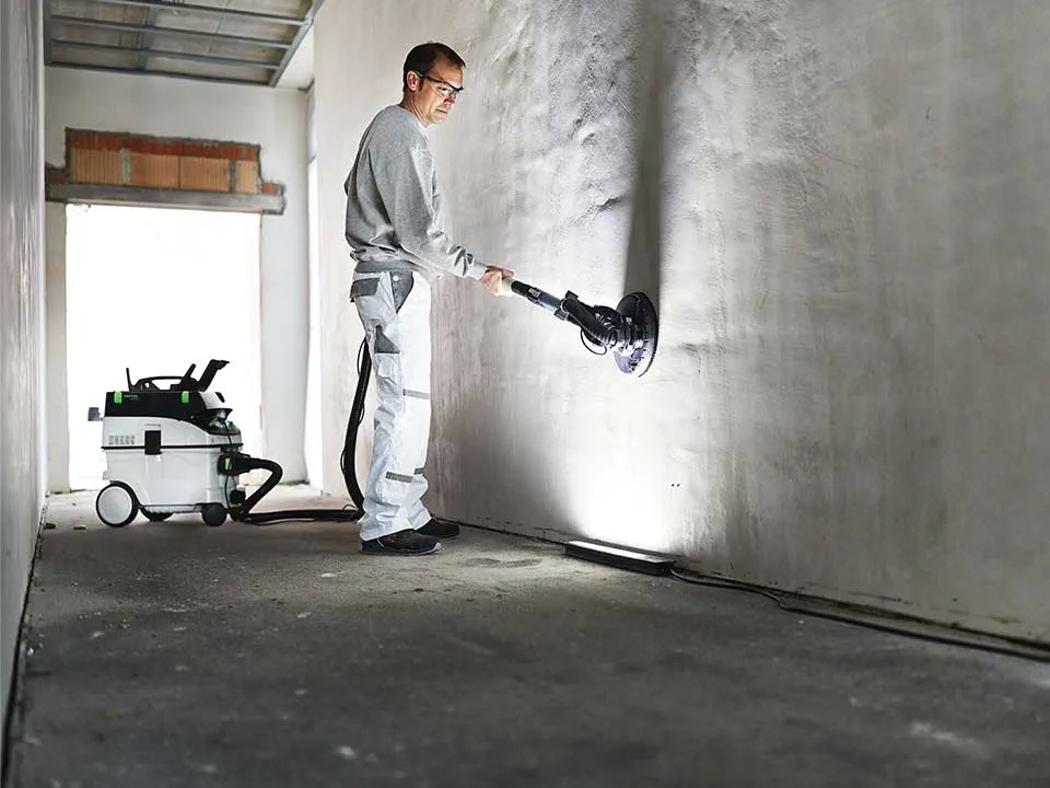 Meistars ar Virsmu pārbaudes lukturi izgaismo sienu un slīpē to.